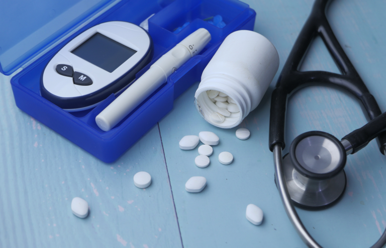 Blood glucose meter, lancet device, medication pills, and a stethoscope arranged on a blue surface, representing diabetes management.