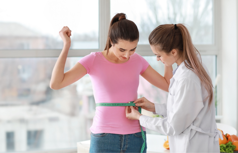 Healthcare professional measuring a woman’s waist with a tape measure during a weight management consultation.