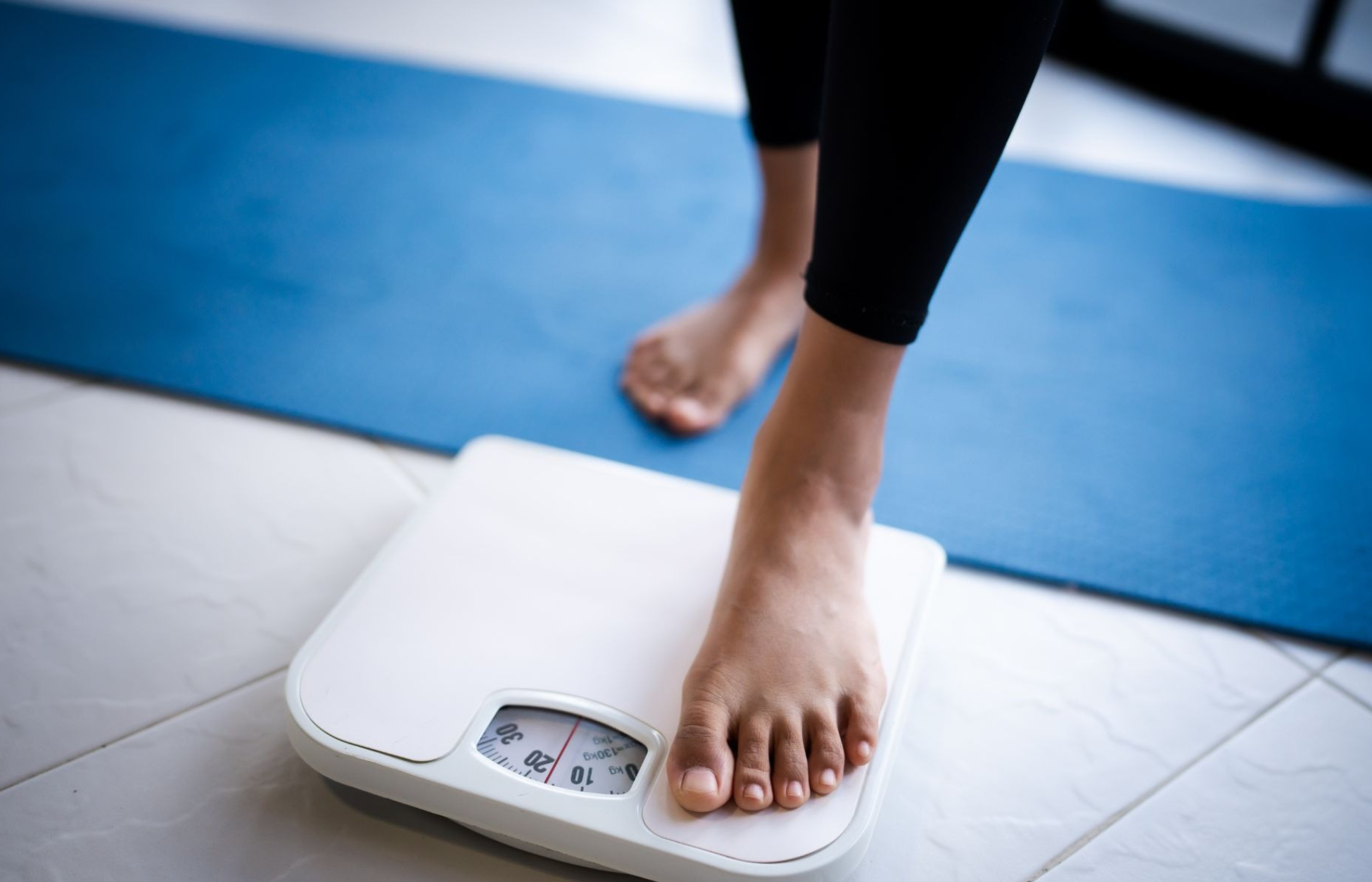 Person stepping onto a bathroom scale to monitor weight loss progress.