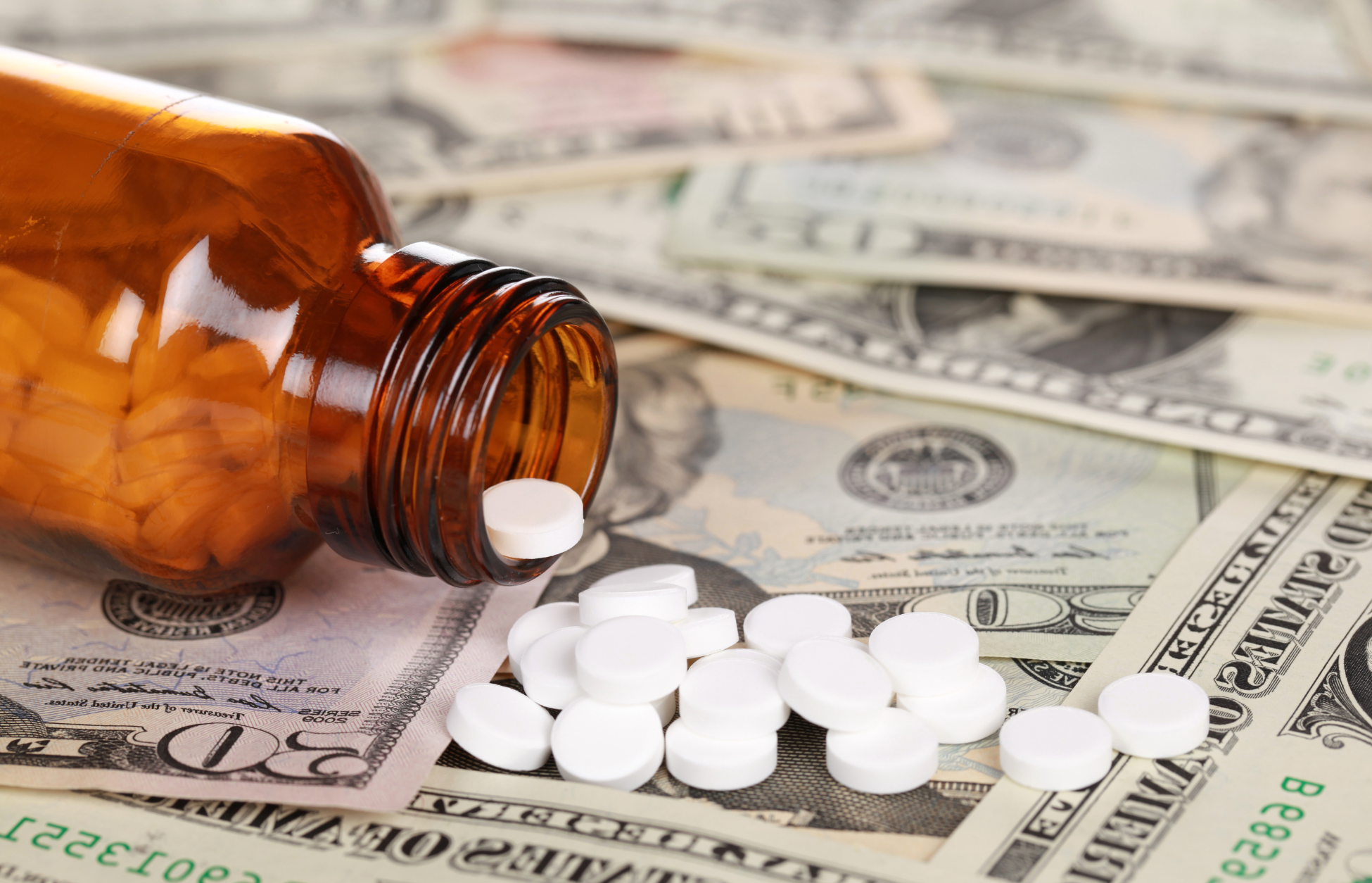 Prescription pills spilling from an amber medicine bottle onto U.S. dollar bills, symbolizing medication costs and healthcare spending.