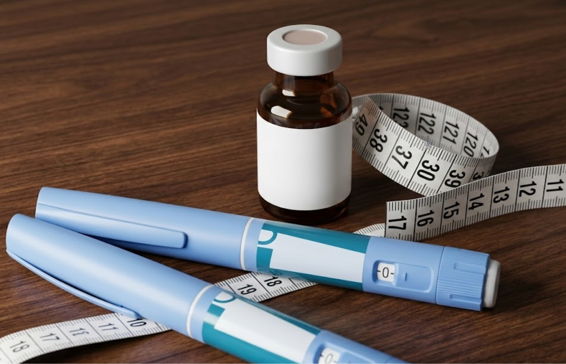 Two GLP-1 injection pens, a medicine vial, and a measuring tape on a wooden surface, representing weight-loss treatment.