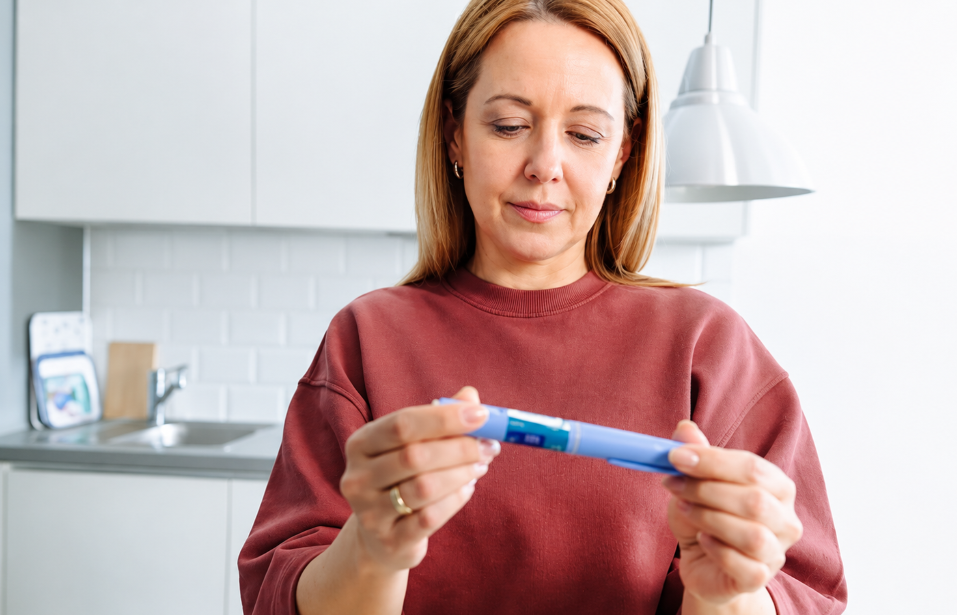 Woman holding and examining a GLP-1 injection pen in a bright home kitchen, illustrating self-administered weight loss medication.