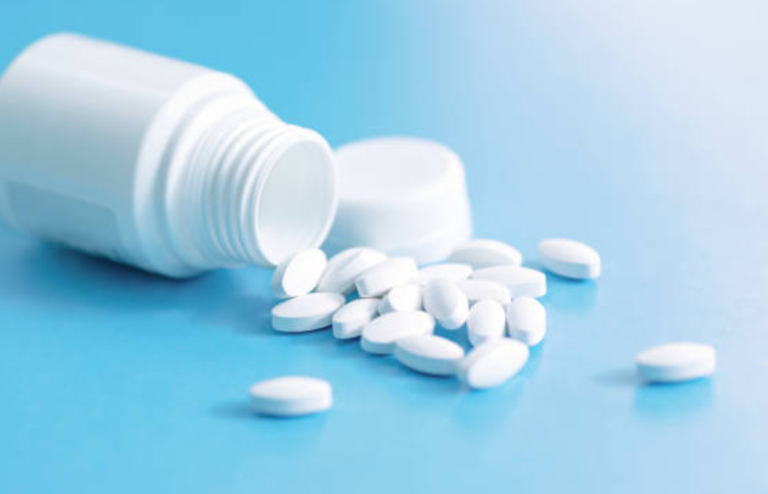 White plastic pill bottle tipped over with several white tablets spilled onto a light blue surface.