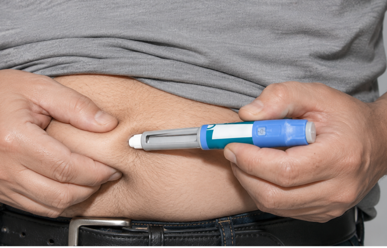 Person in a gray shirt using an injection pen on the abdomen.