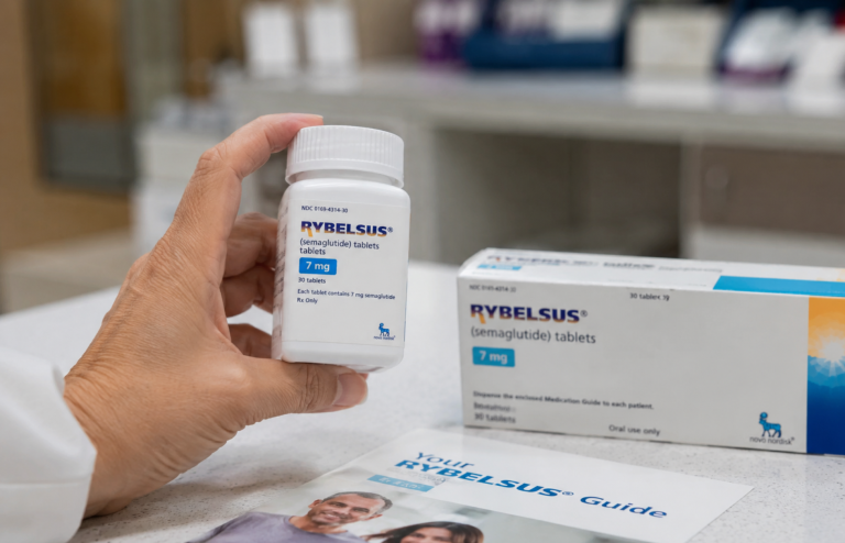 Hand holding a bottle of Rybelsus tablets in a clinical setting with medication packaging nearby.