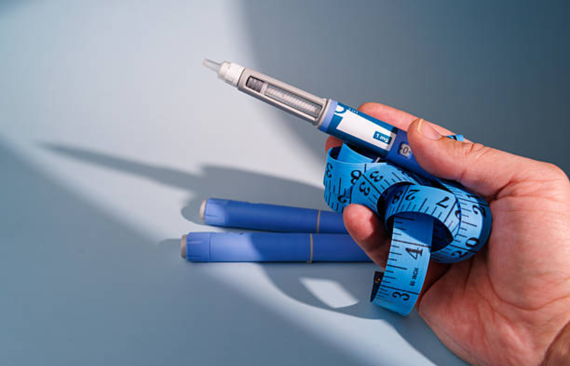 Hand holding a semaglutide injection pen wrapped with a measuring tape, symbolizing weight-loss medication and dosing.