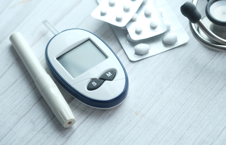Blood glucose meter, insulin pen, medication bottle, scattered tablets, and stethoscope used for type 2 diabetes management.