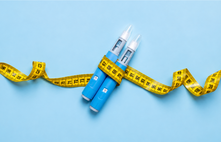 Two blue injectable weight-loss pens wrapped with a yellow measuring tape on a light blue background.