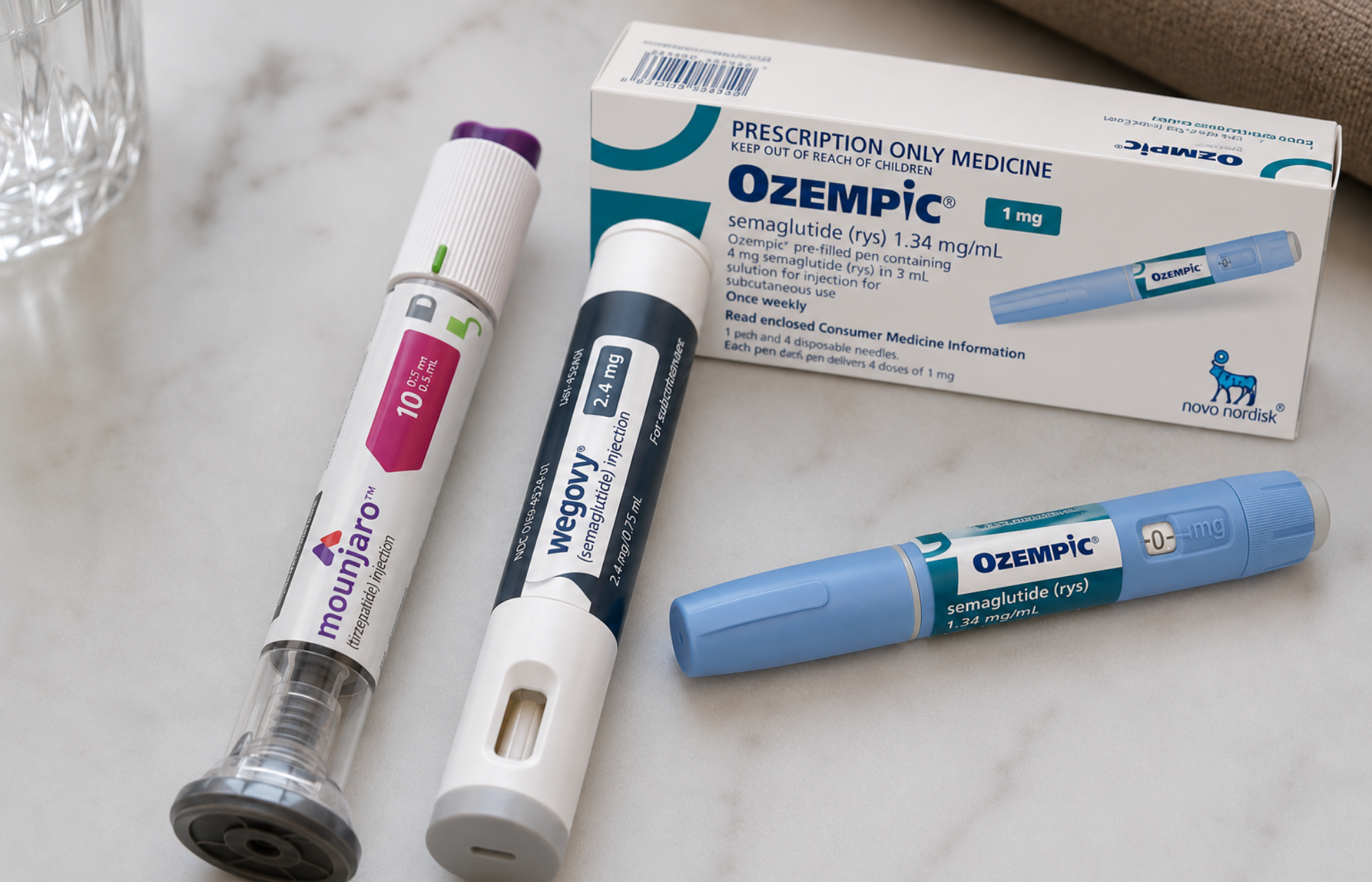 Ozempic medication box with Ozempic, Wegovy, and Mounjaro injection pens on a marble surface.